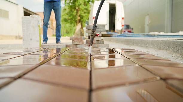 Person cutting brown tiles with a saw outdoors, white van in the background.