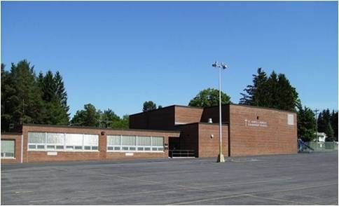 Low brick school building with a parking lot and tall light pole under a clear blue sky