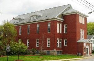 Red brick building with gray roof and white trim on a corner lot with grass and trees