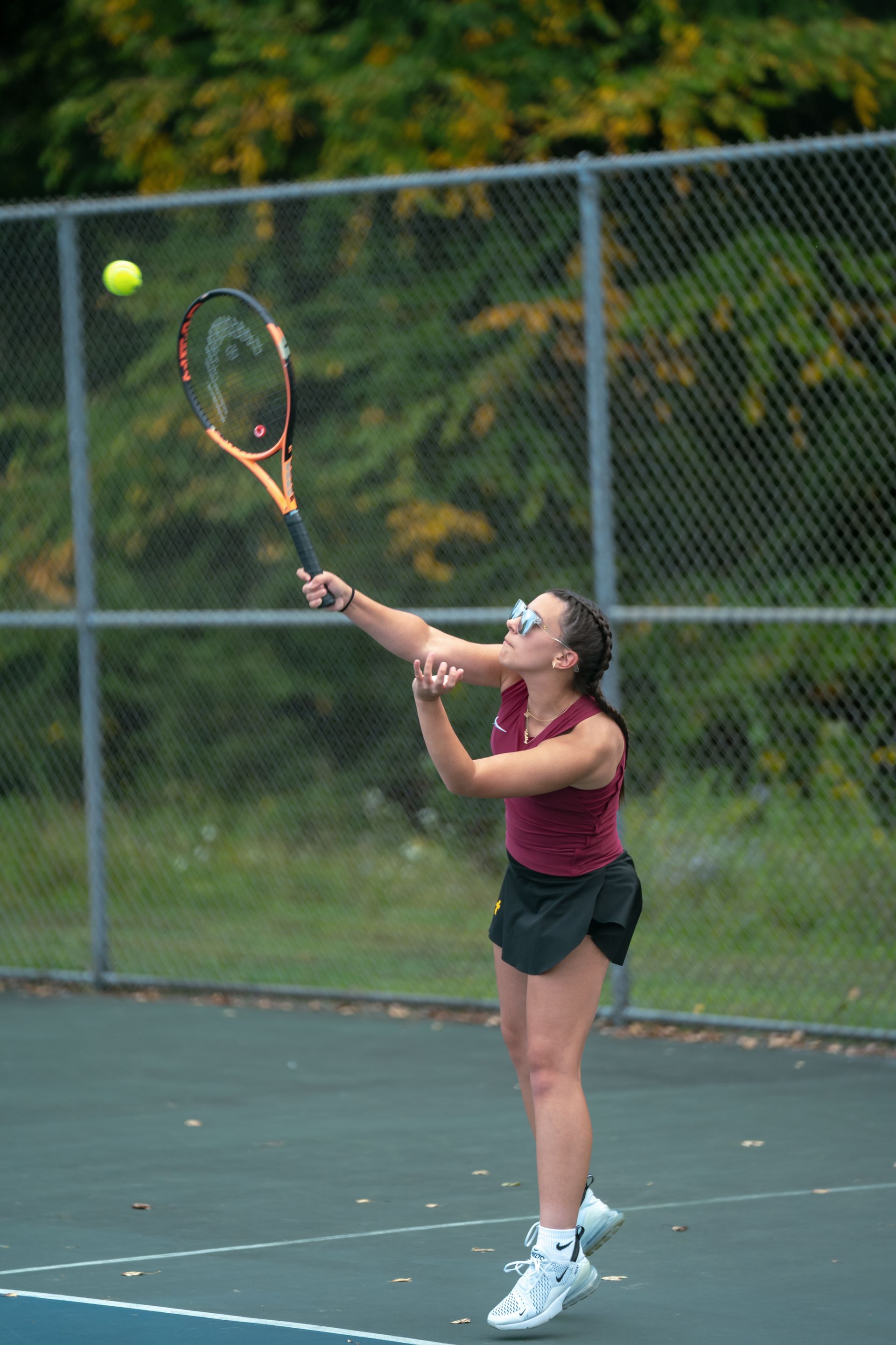 Tennis player in maroon shirt serving on an outdoor court, with racket raised and ball in the air