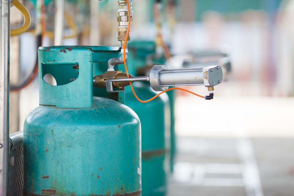 Teal Gas Cylinders Lined Up in a Filling Station With Automated Metal Nozzles — PlumbPlus in Kawana, QLD