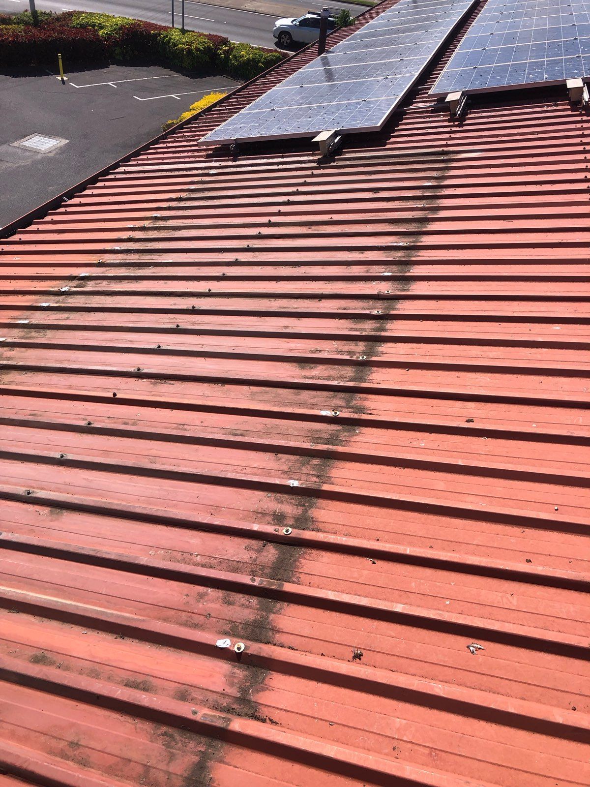 A Red Metal Roof With a Dark Streak of Grime Underneath Solar Panels — PlumbPlus in Kawana, QLD