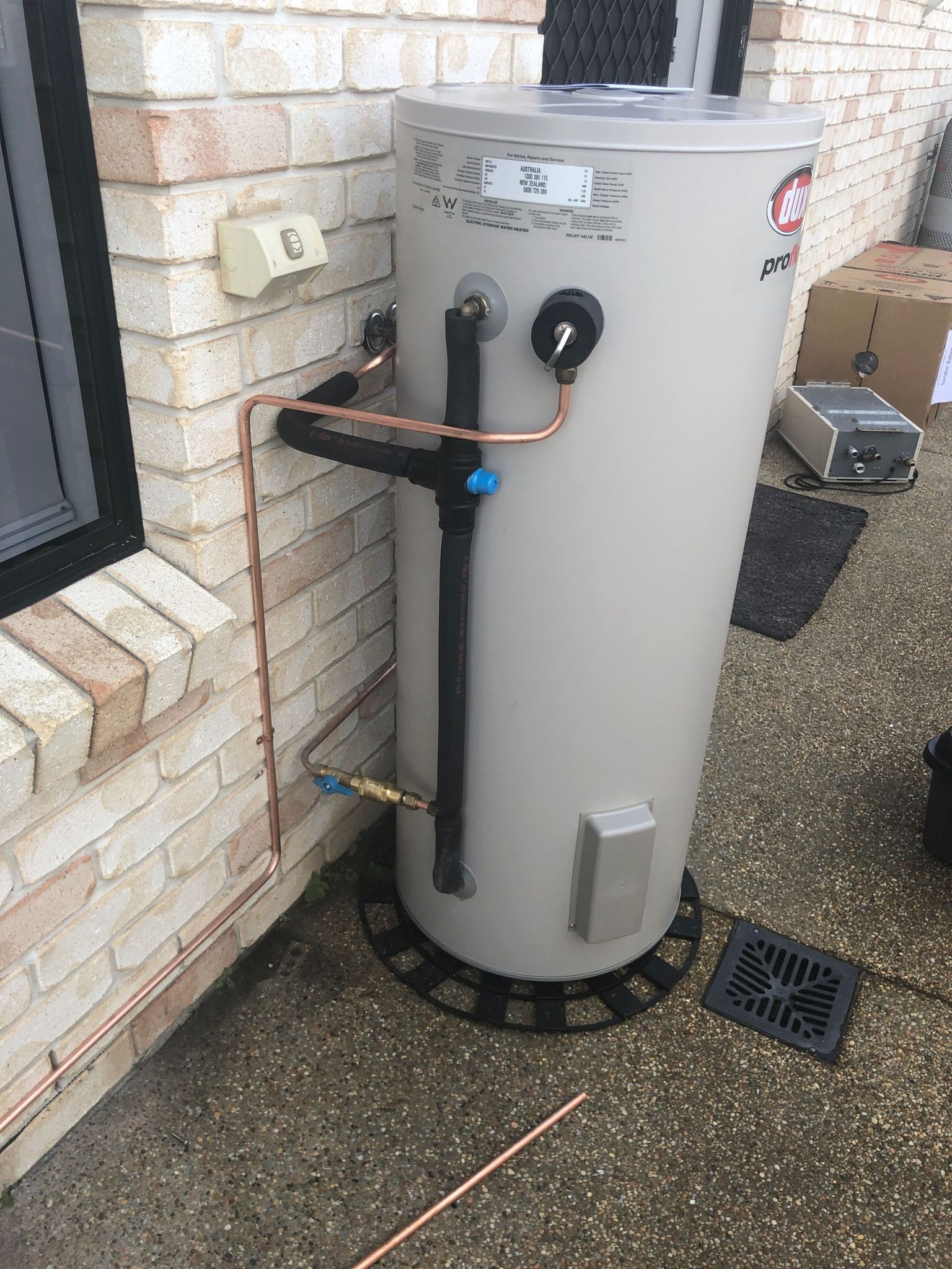 Outdoor water heater tank beside a brick wall, with pipes and valves connected. — PlumbPlus in Kawana, QLD