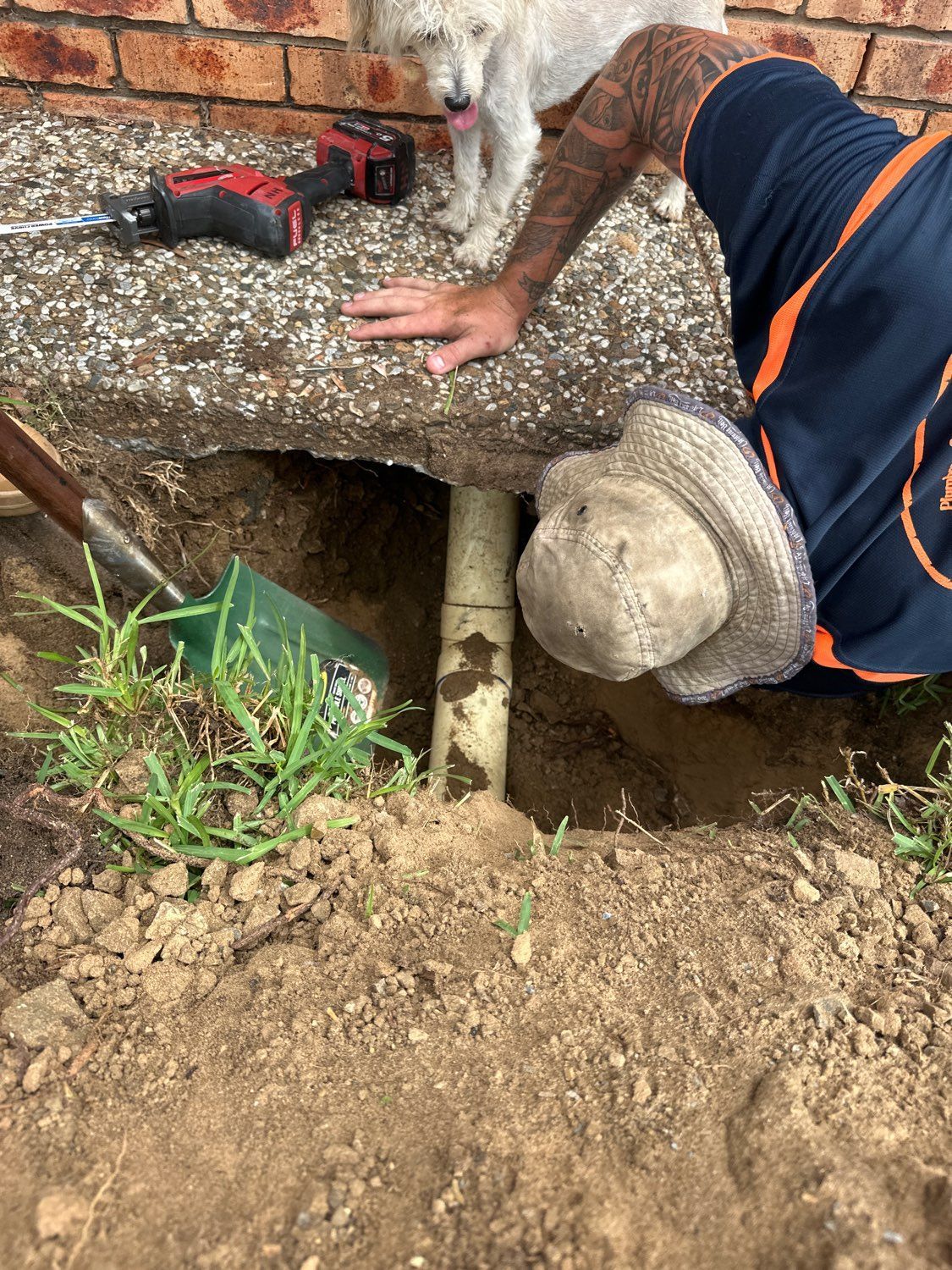 A Person in a Sun Hat Reaches Into a Hole Dug Beneath Concrete to Inspect a Pipe — PlumbPlus in Kawana, QLD