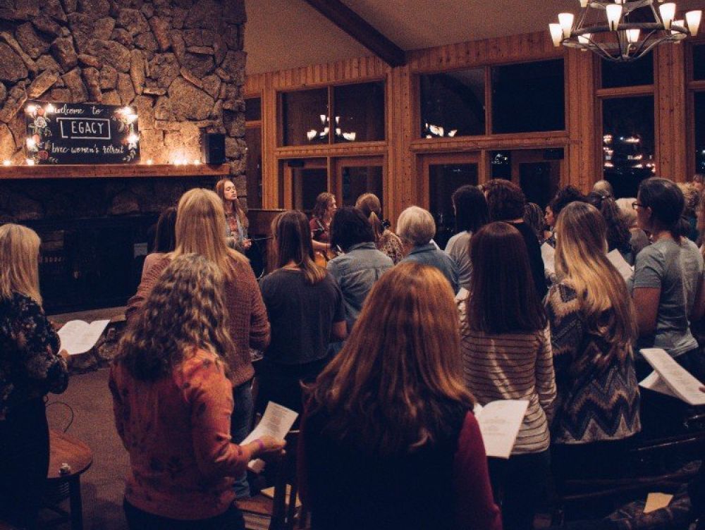 A large group of people are singing in a room with a sign that says