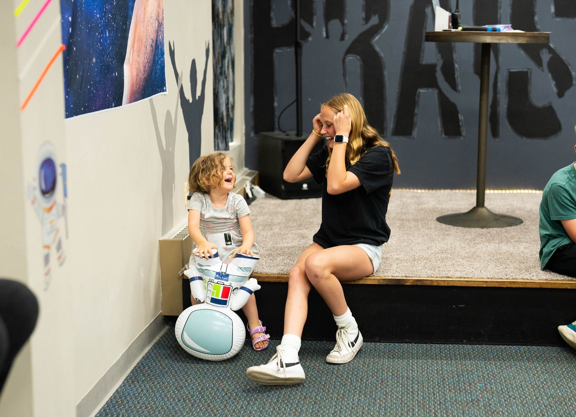 A woman and a little girl are sitting on a stage playing drums.