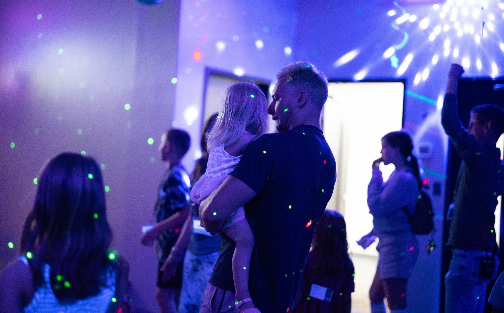 A man is holding a little girl in his arms at a party.
