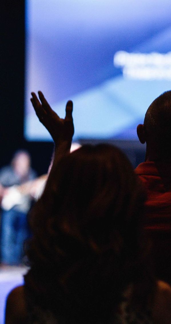 A group of people are sitting in front of a screen with their hands in the air.