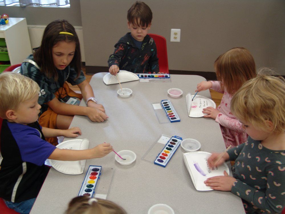 A group of children are sitting around a table playing with watercolors