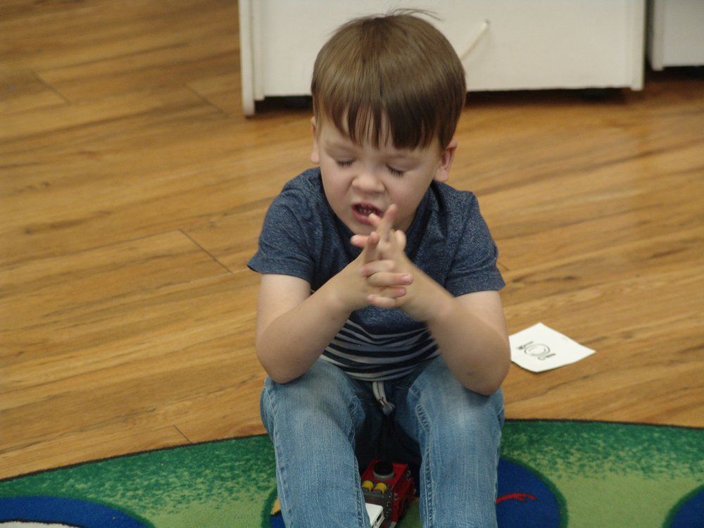A young boy is sitting on the floor with his hands folded in prayer.