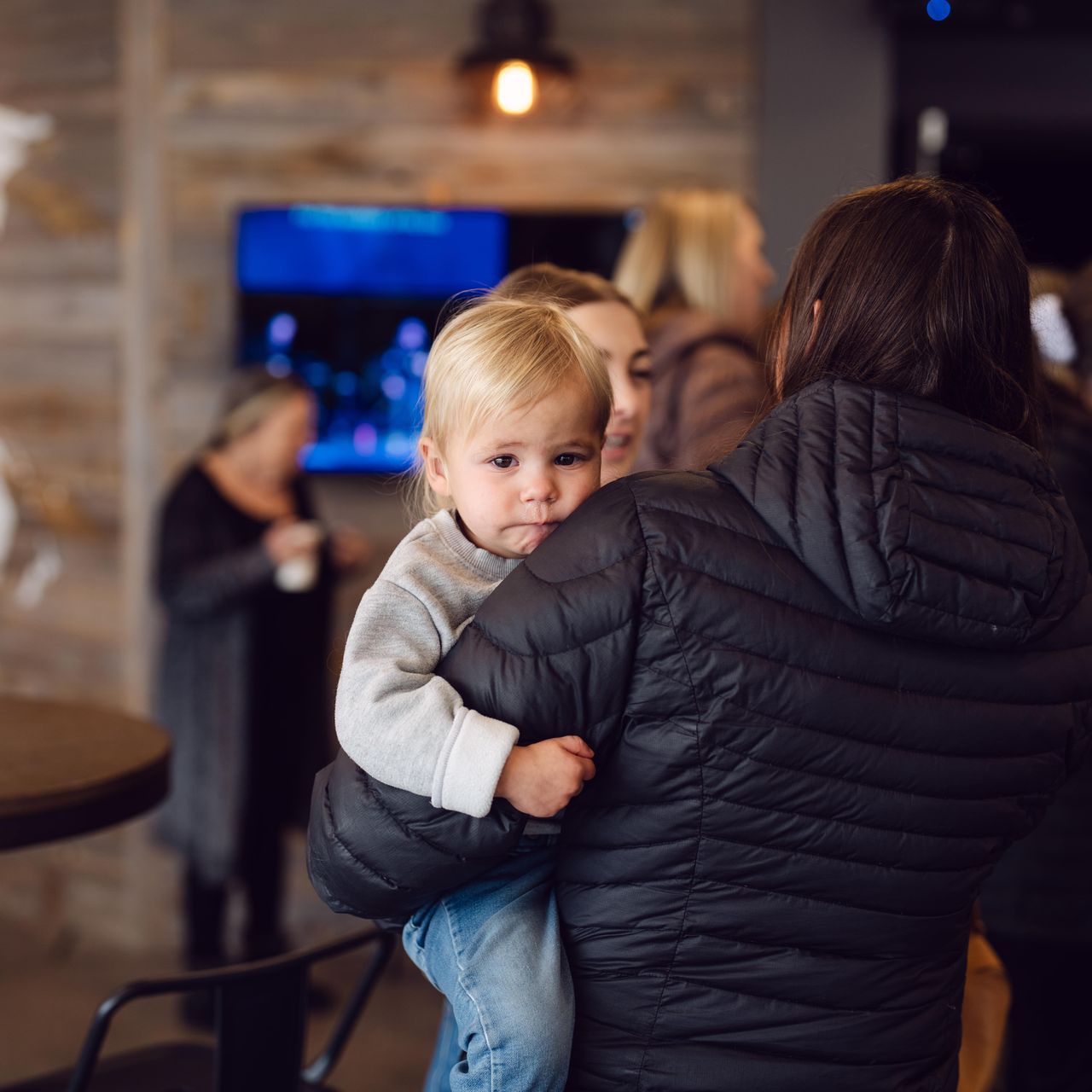 A woman in a black jacket is holding a baby in her arms