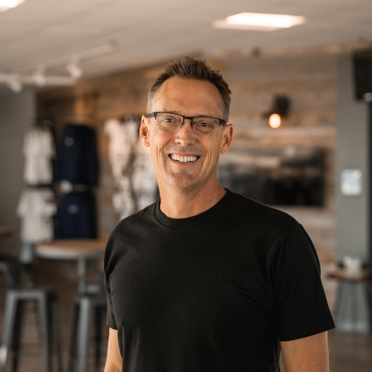 A man wearing glasses and a black shirt is smiling for the camera.