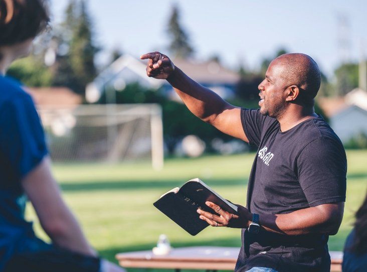 A man is holding a bible and pointing at something while talking to a group of people.