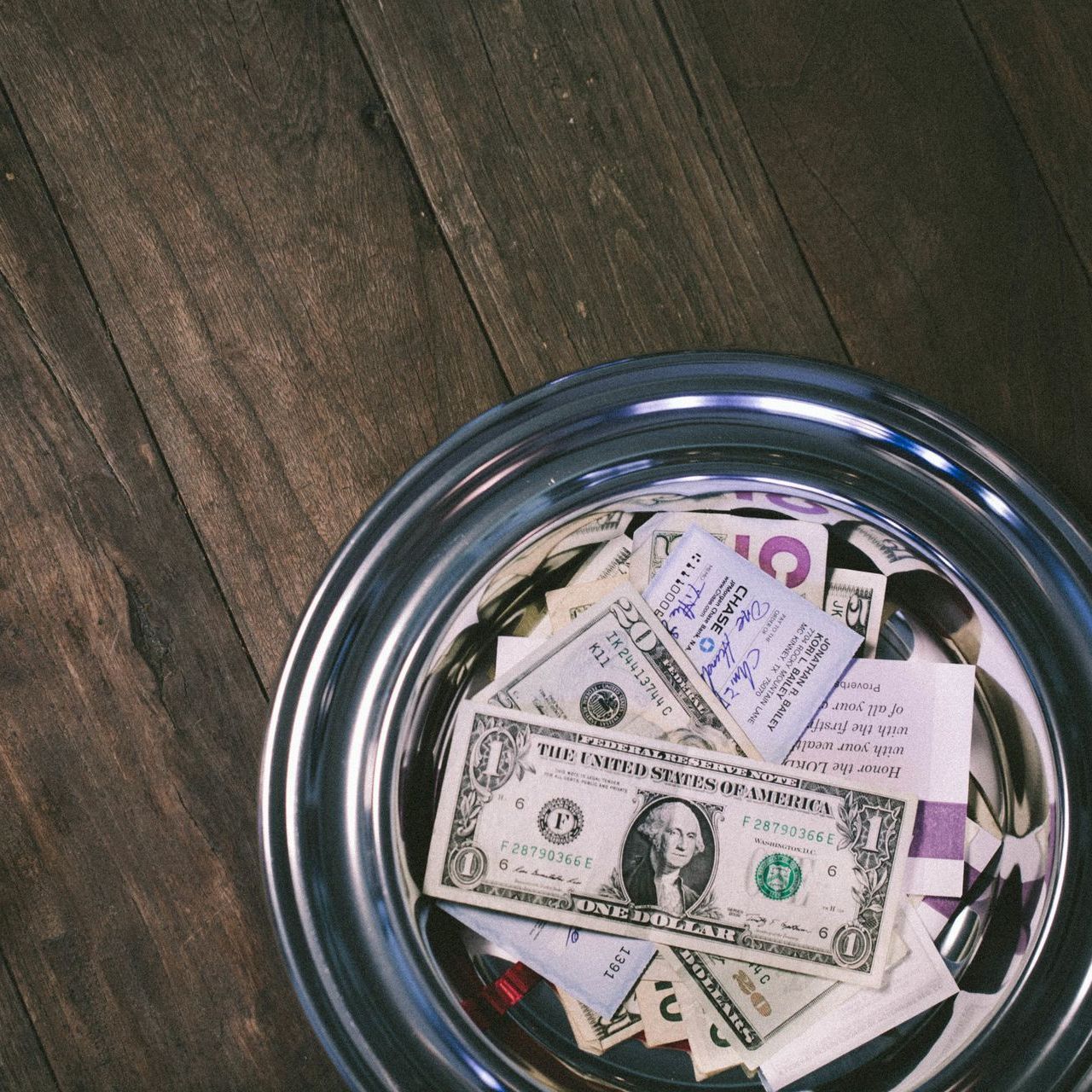 A silver bowl filled with dollar bills including a one dollar bill