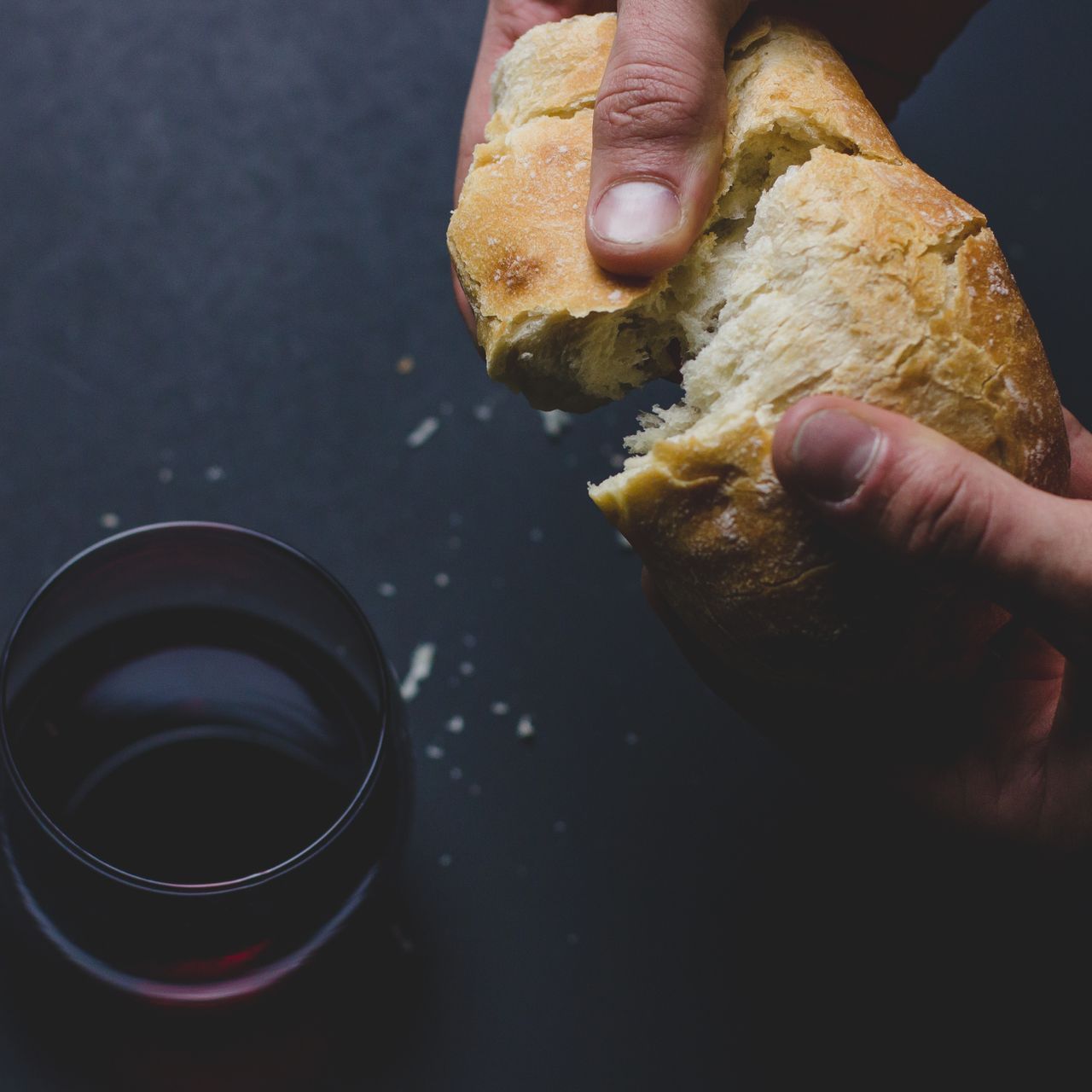 A person is holding a piece of bread next to a glass of wine