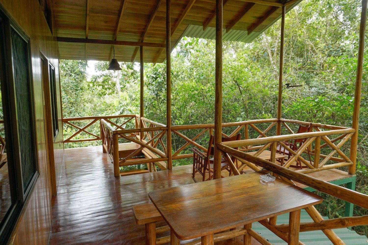 Wooden porch with table, chairs, and railing, overlooking a lush green forest.