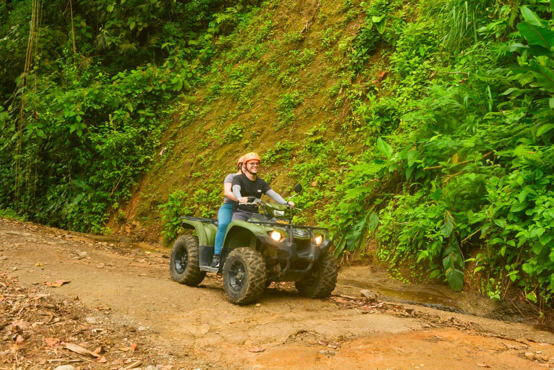 Person riding an ATV on a muddy road through a lush green jungle.