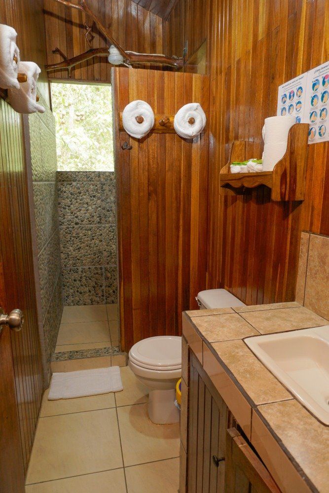 Wooden-paneled bathroom with toilet, sink, shower, and towels.