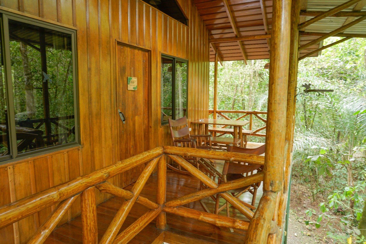 Wooden cabin with porch overlooking lush green foliage.