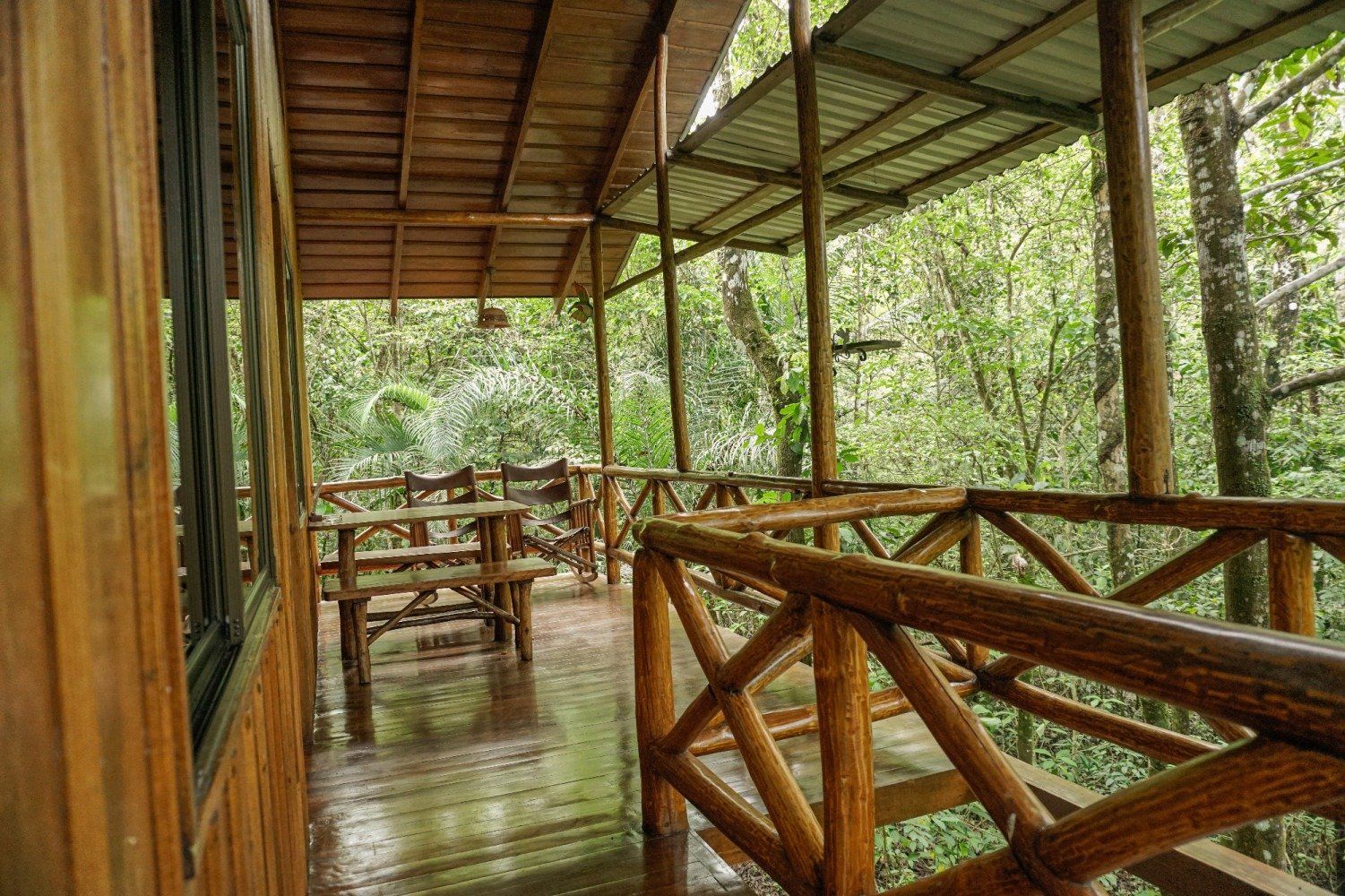 Wooden porch with tables, chairs, and railing overlooking lush green forest.