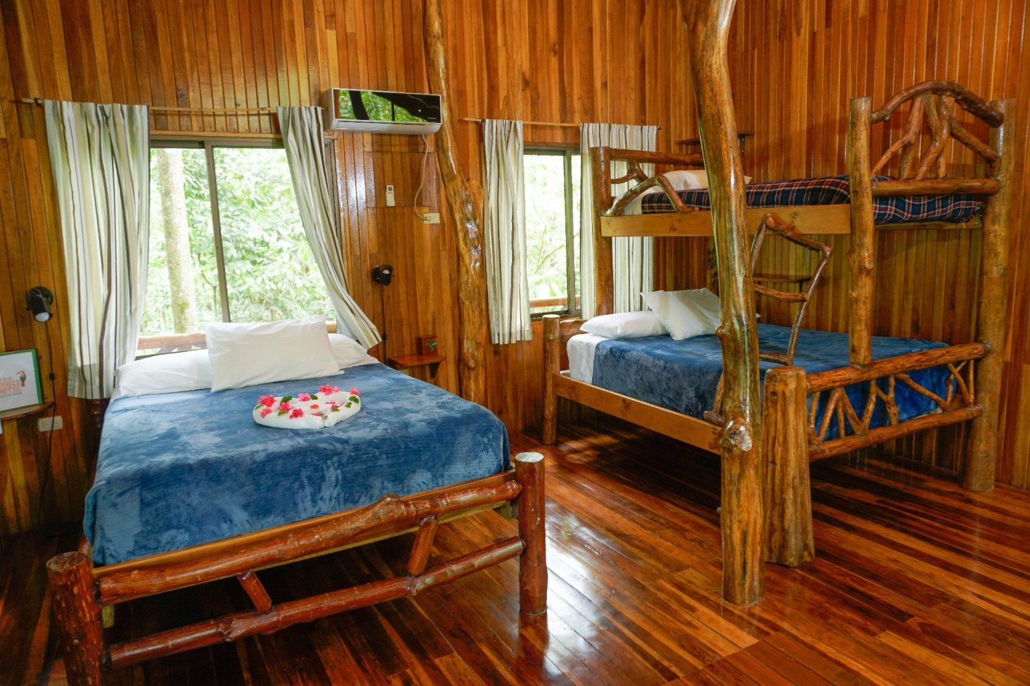 Wooden bedroom with a double bed and bunk beds; windows with forest view.