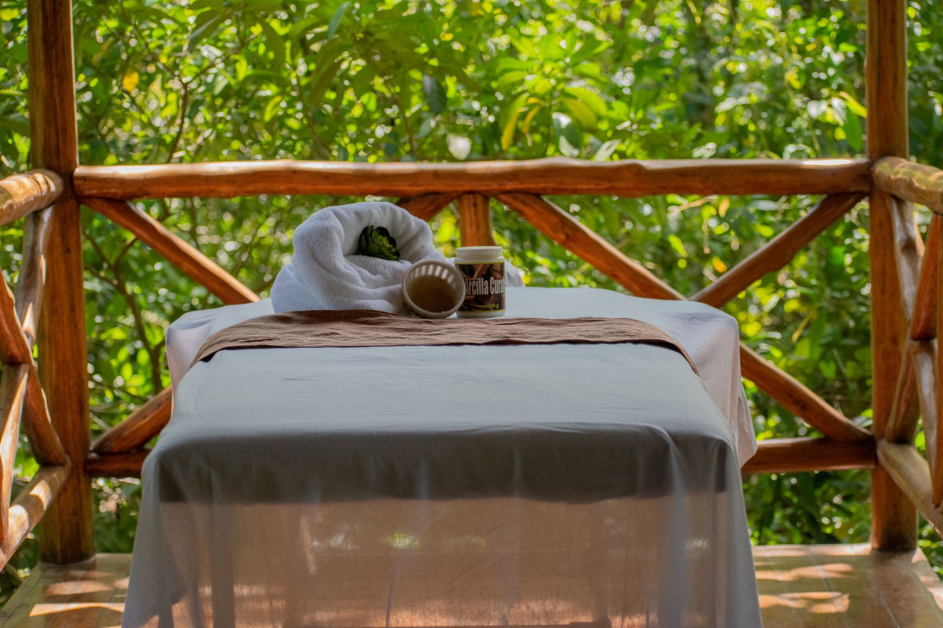Massage table on a wooden deck, surrounded by lush green foliage, with spa products.
