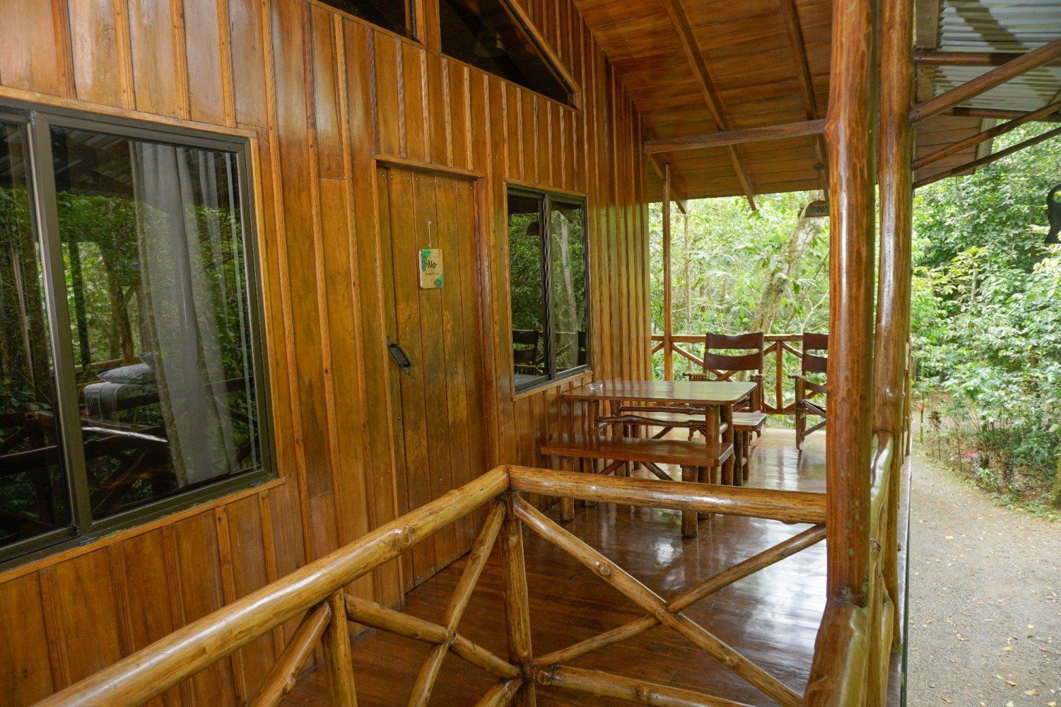 Wooden cabin exterior with porch, table, chairs. Windows, door, railings, and forest view.
