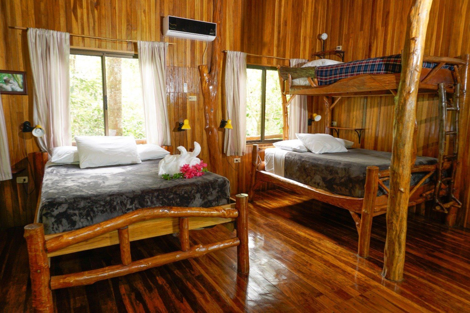 Wooden cabin interior with two beds, a bunk bed, and two windows.