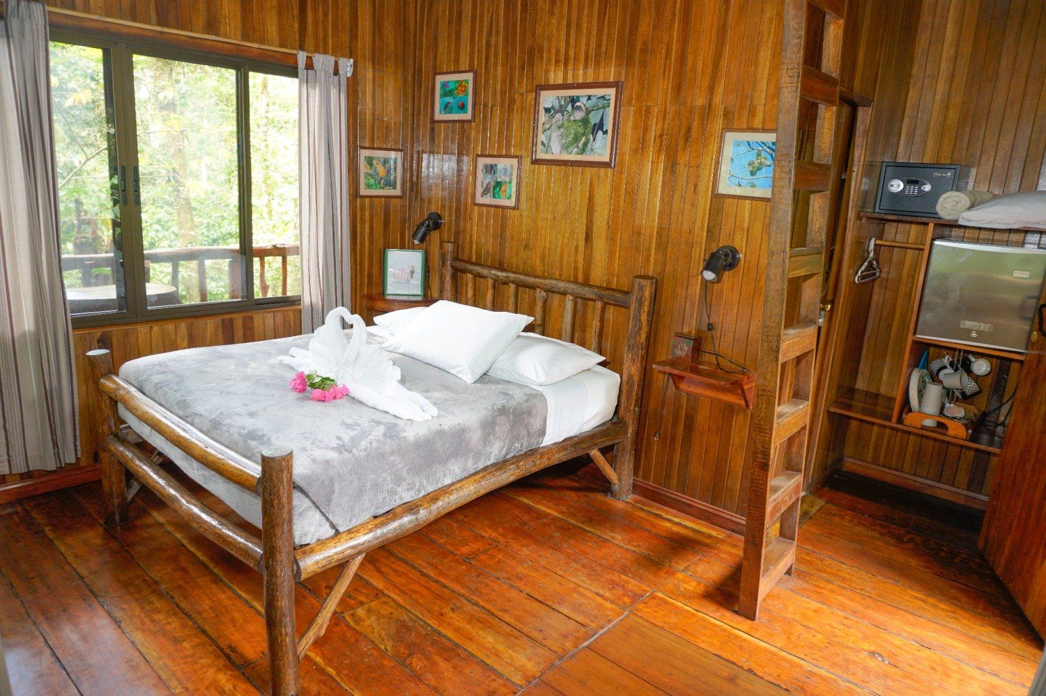 Cozy wood-paneled bedroom with a double bed decorated with towels. Window with forest view.