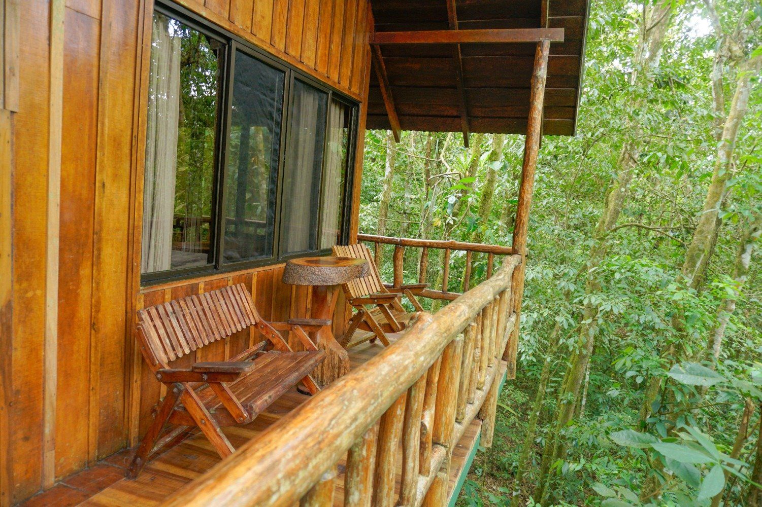 Wooden balcony with seating overlooking lush green forest.