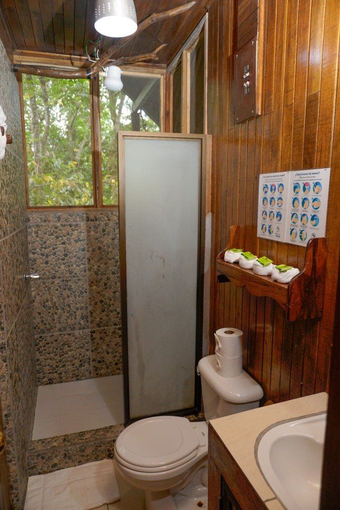 Small wooden bathroom with shower, toilet, sink, and instructional poster.