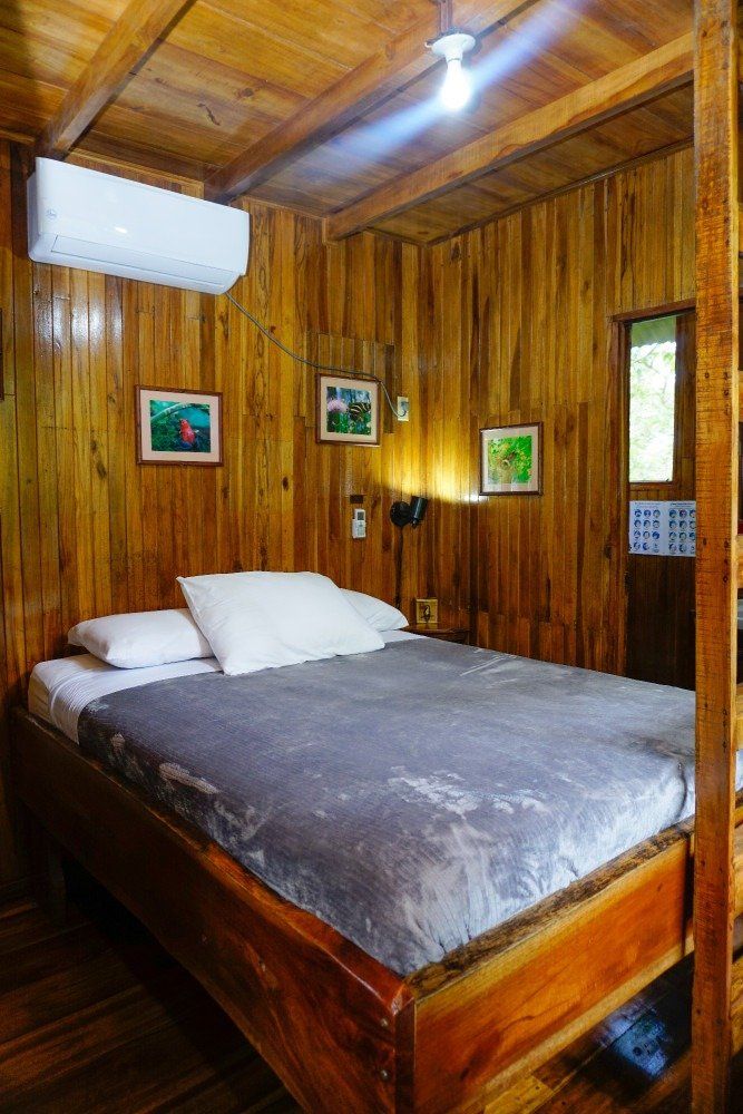 Wooden bedroom with a bed, air conditioner, and small framed art.