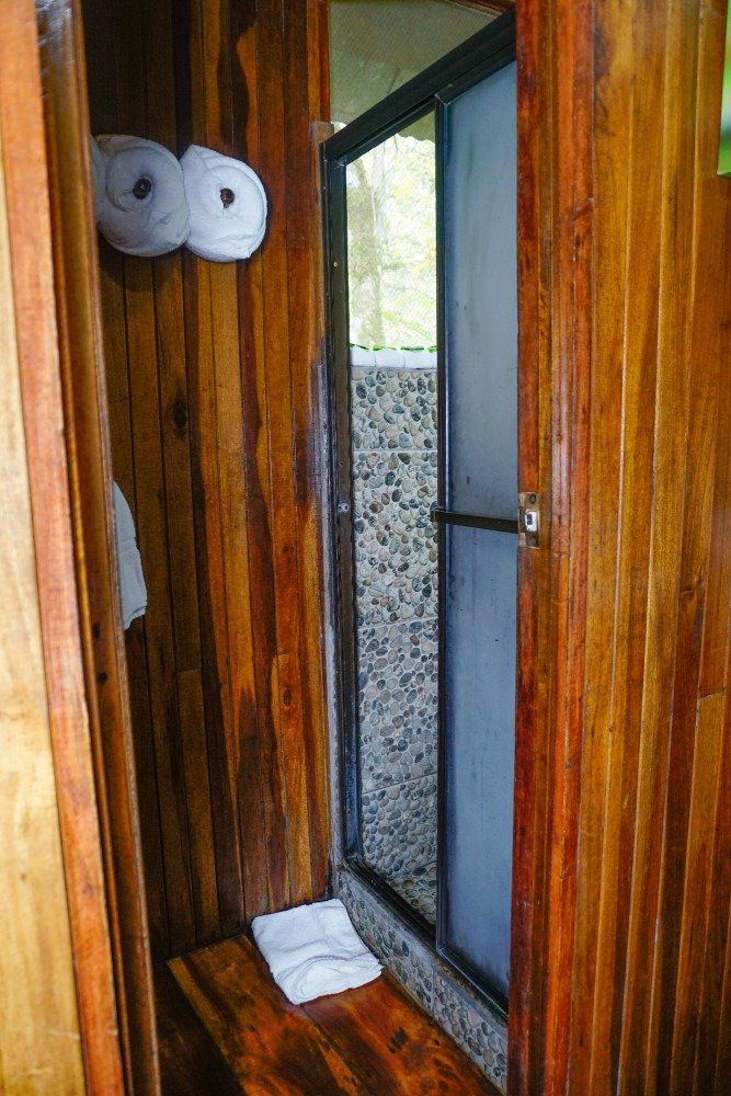 Wooden shower stall with sliding glass door, towels, and bench.
