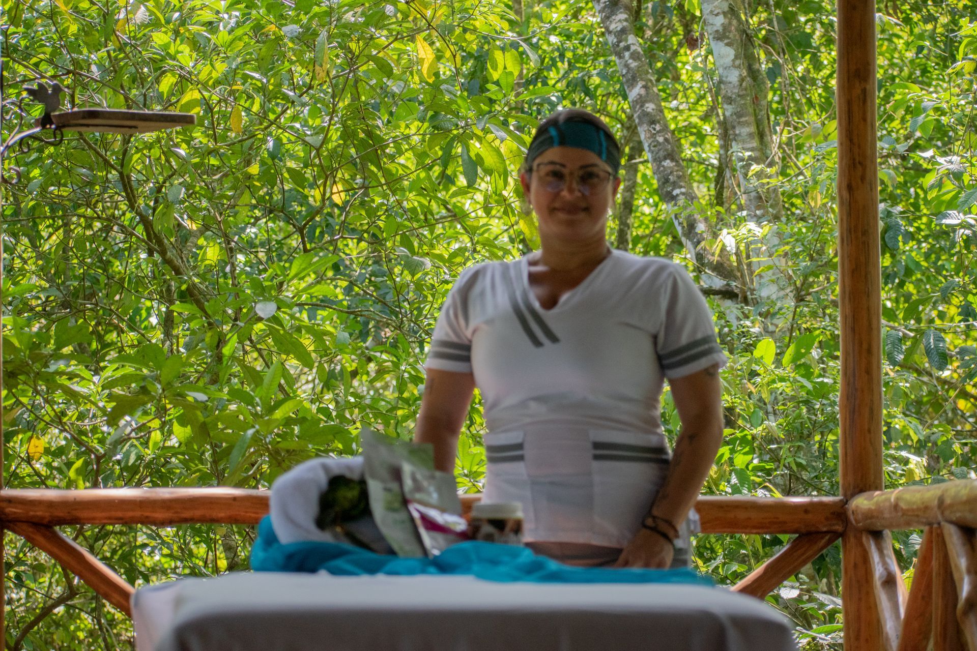 Woman in white uniform stands at a massage table in a lush, green outdoor setting.