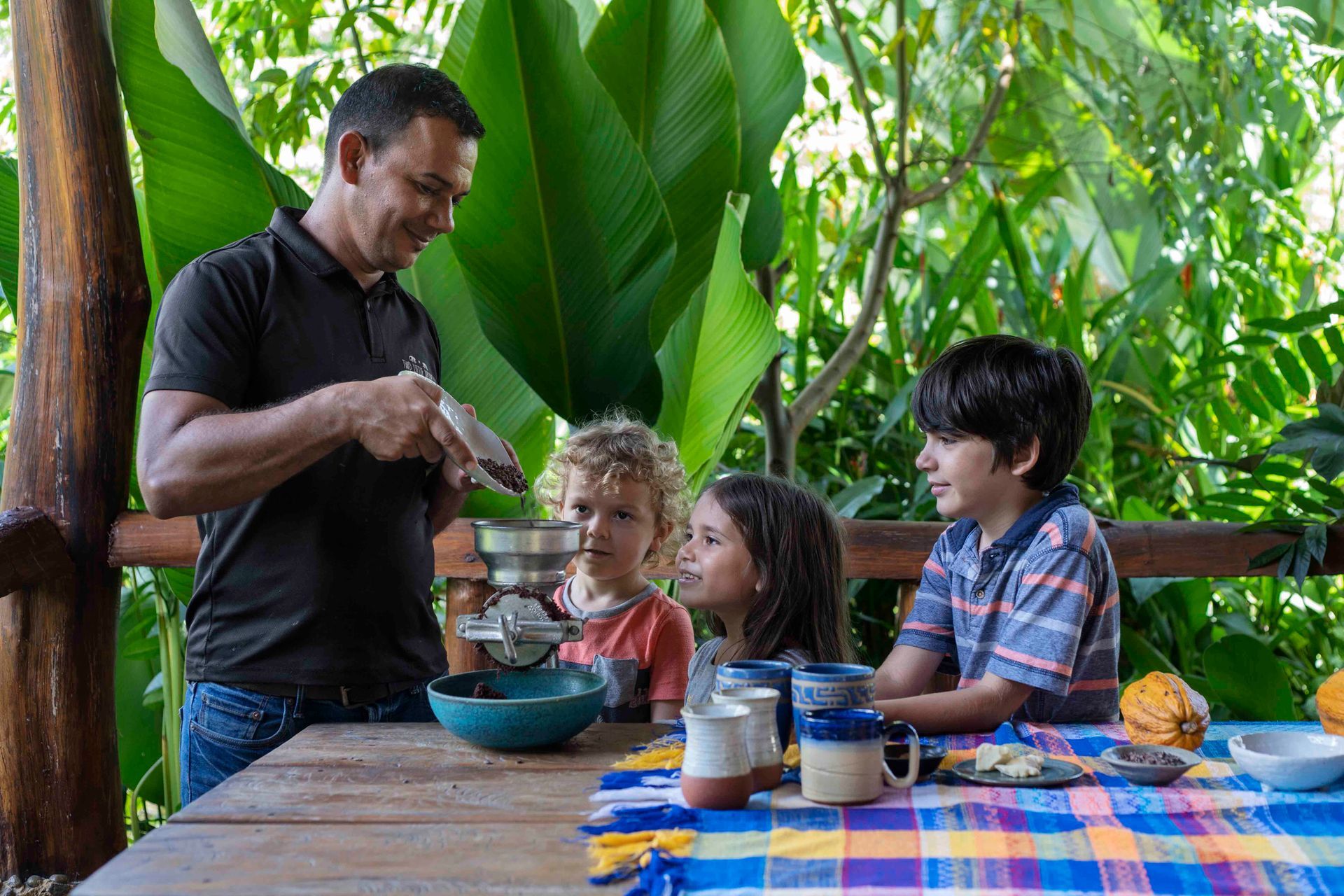 Man making chocolate for children on a wooden table outdoors. Green foliage.