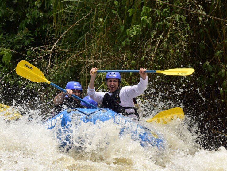 People whitewater rafting, one cheering with paddles, water splashing.