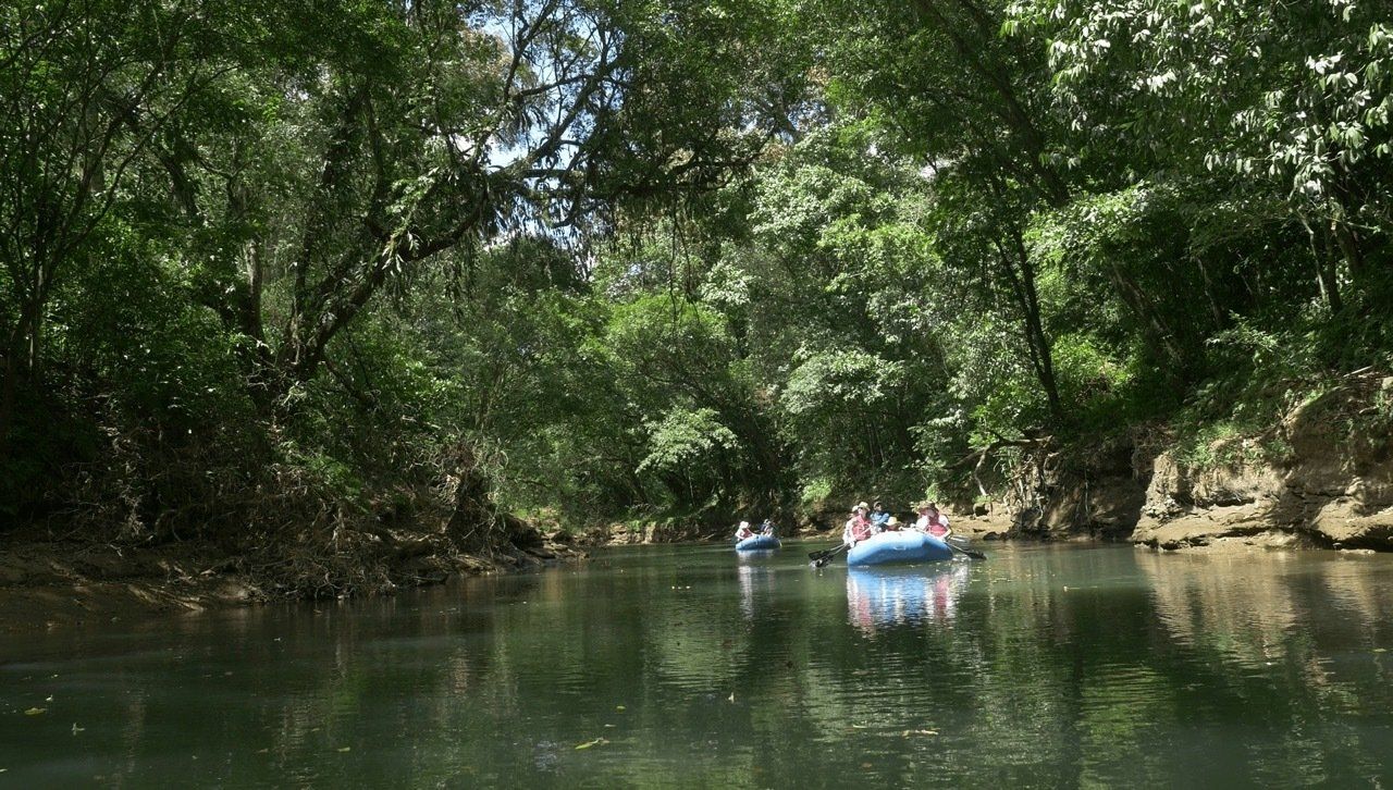 Rafting on a shaded river, surrounded by green trees.