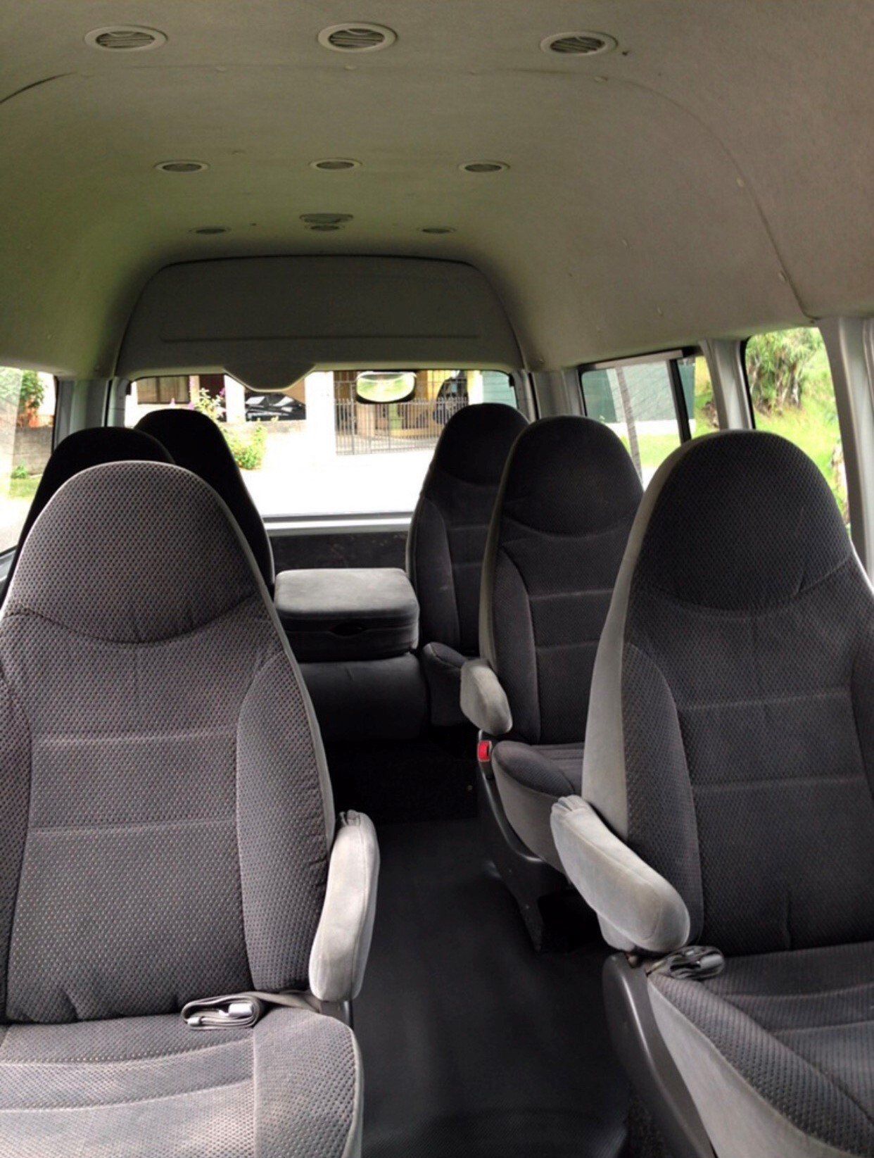 Interior of a passenger van with gray seats, a black floor, and a light-colored ceiling.