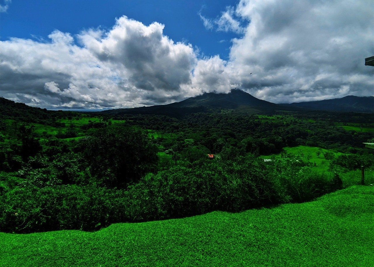 Lush green landscape with forest, mountains, and partly cloudy blue sky.