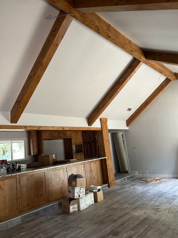 Rustic interior with exposed wood beams, white vaulted ceiling, and wood-paneled bar area under renovation