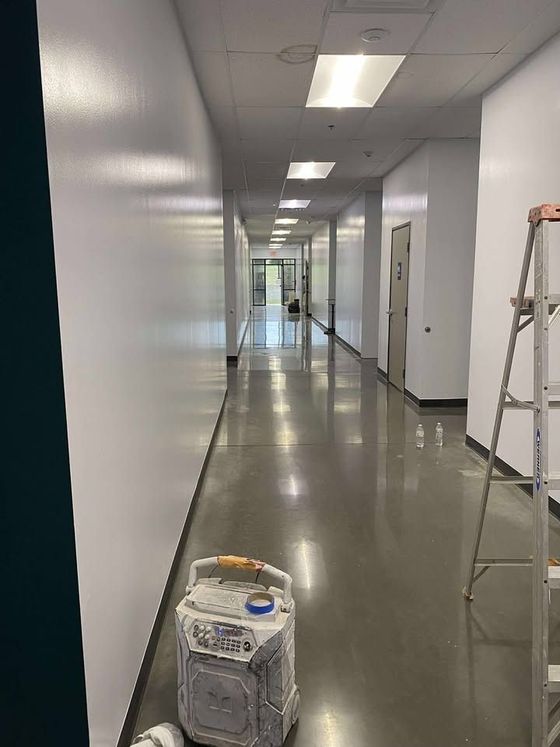 Empty hallway with glossy floors, white walls, a ladder on the right, and a small container in the foreground.