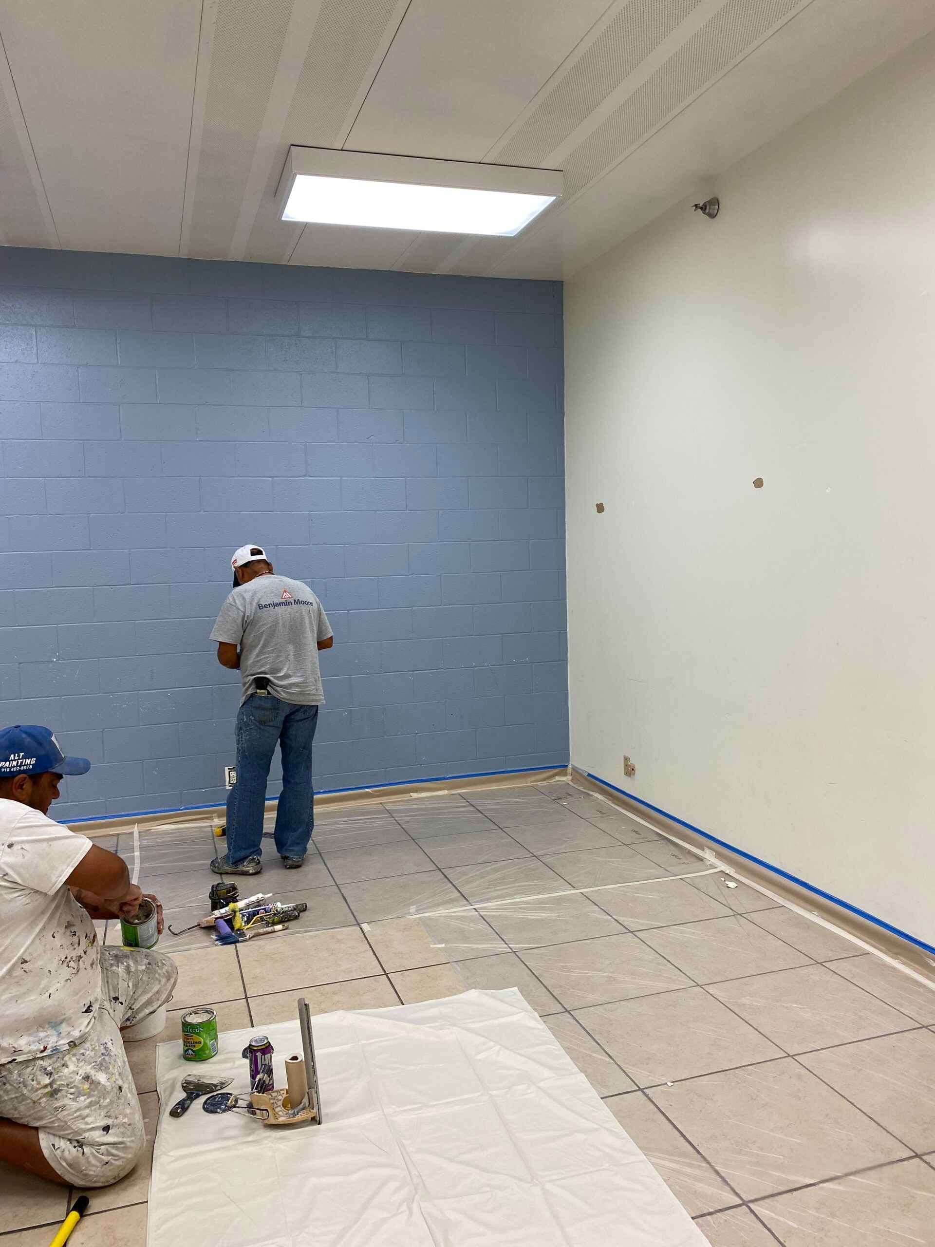 Workers laying tile in a mostly empty room with blue and white walls and tools on the floor