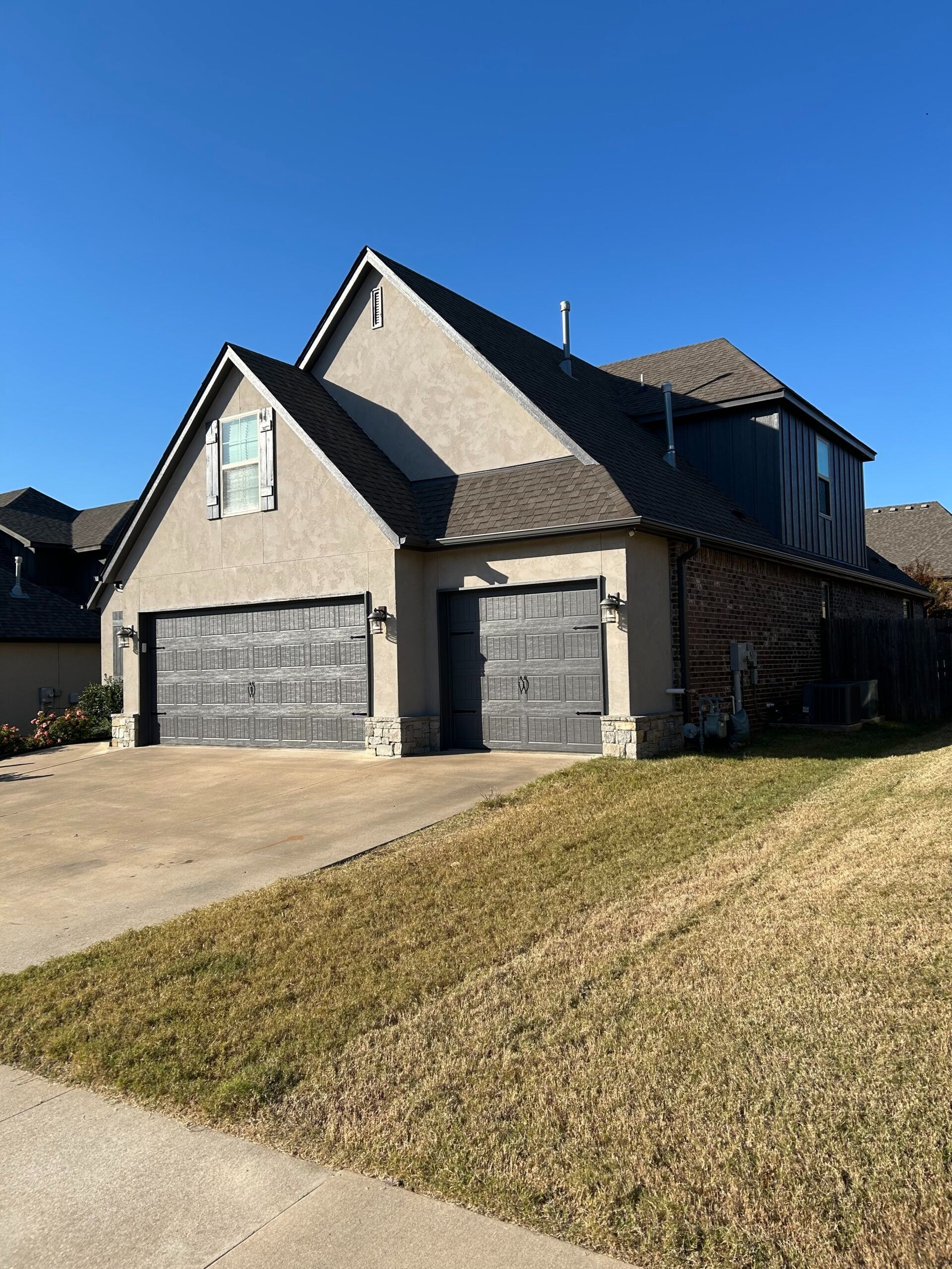 Two-story suburban house with gray brick, gabled roof, and double garage under a clear blue sky