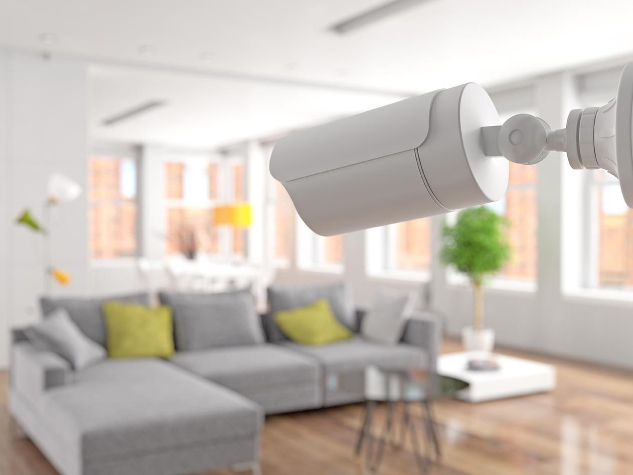 Security camera mounted inside a modern living room with a gray sofa, coffee table, and windows.