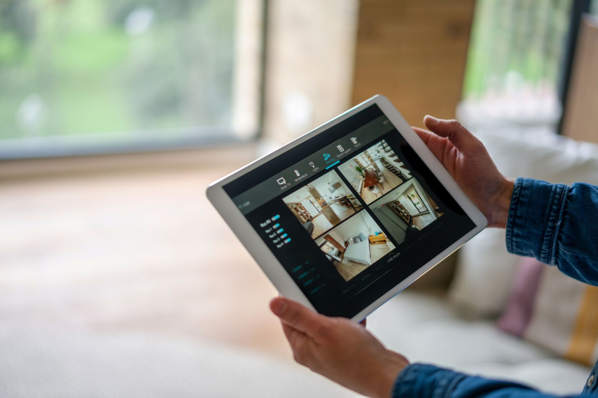 A person is holding a cell phone in front of a security system. Person uses a smartphone and tablet to operate a security system by Honeywell. Devices show green and red icons with a store in the background.