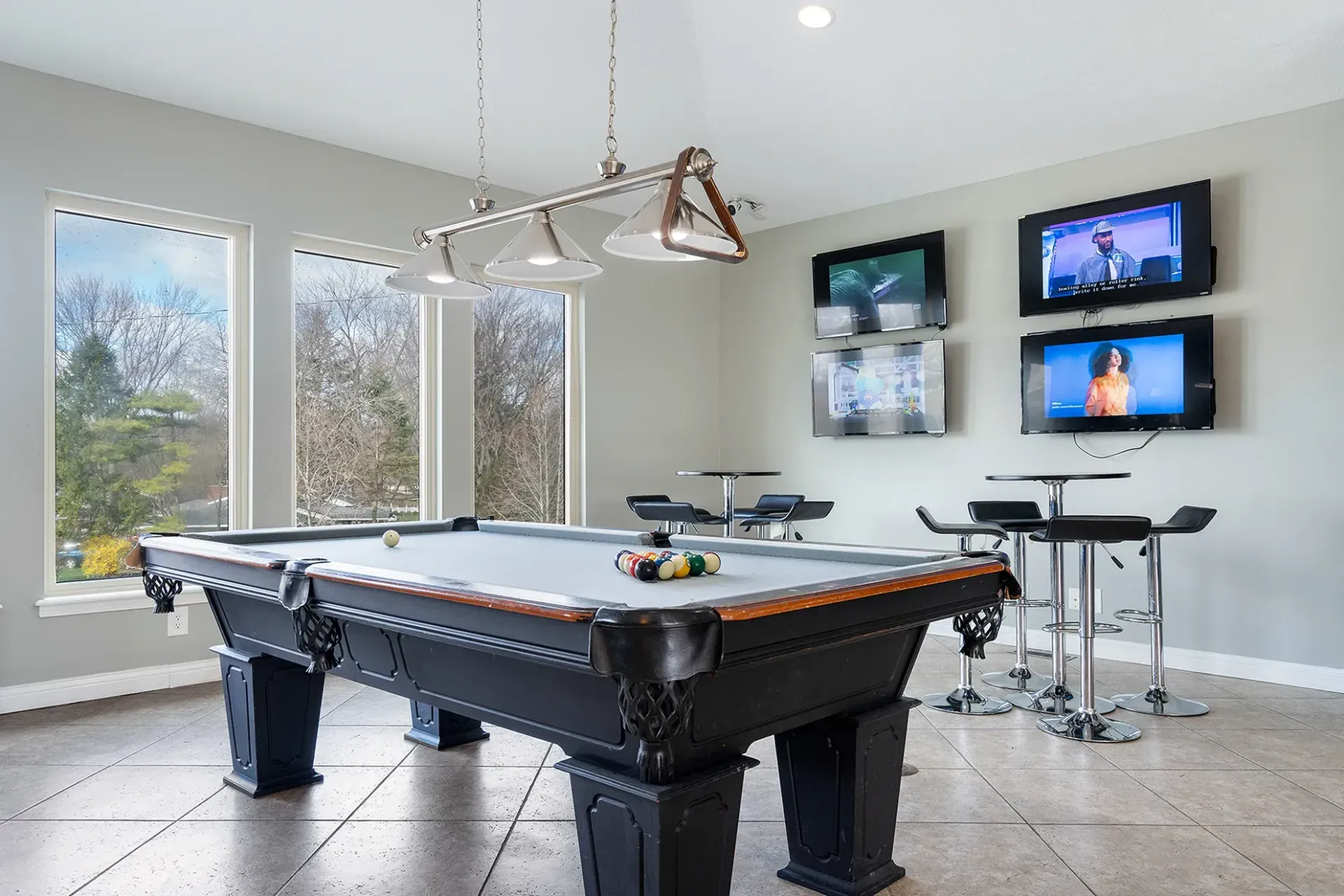 Pool table in a room with multiple mounted TVs, a window with outdoor view, and high-top tables.