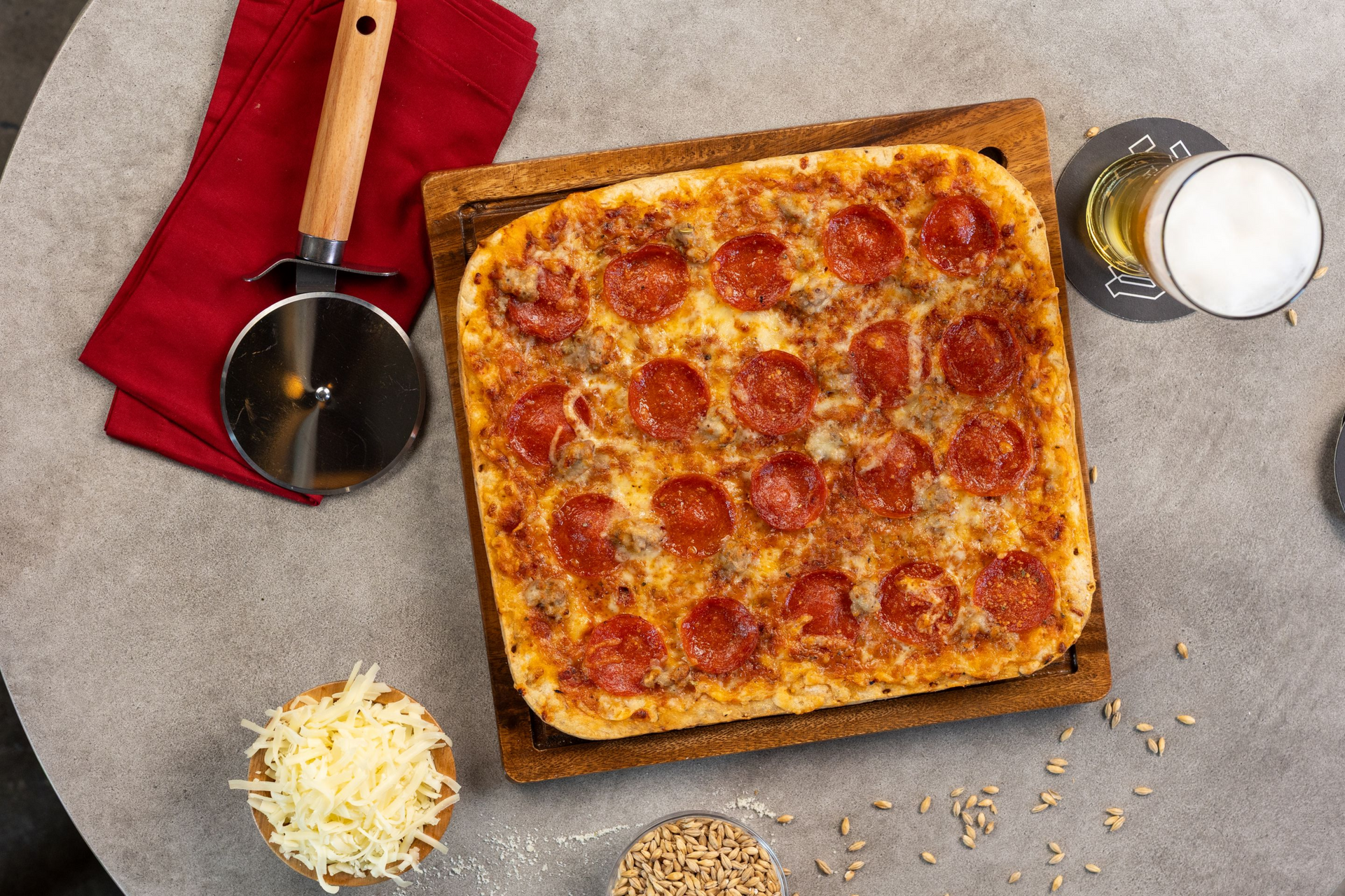 Pepperoni pizza in a square pan with cheese, sauce, and ingredients on a gray table