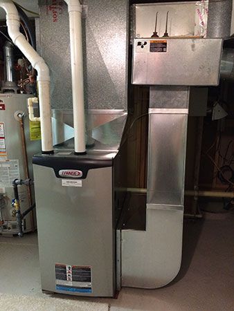 A boiler is sitting in a basement next to pipes.