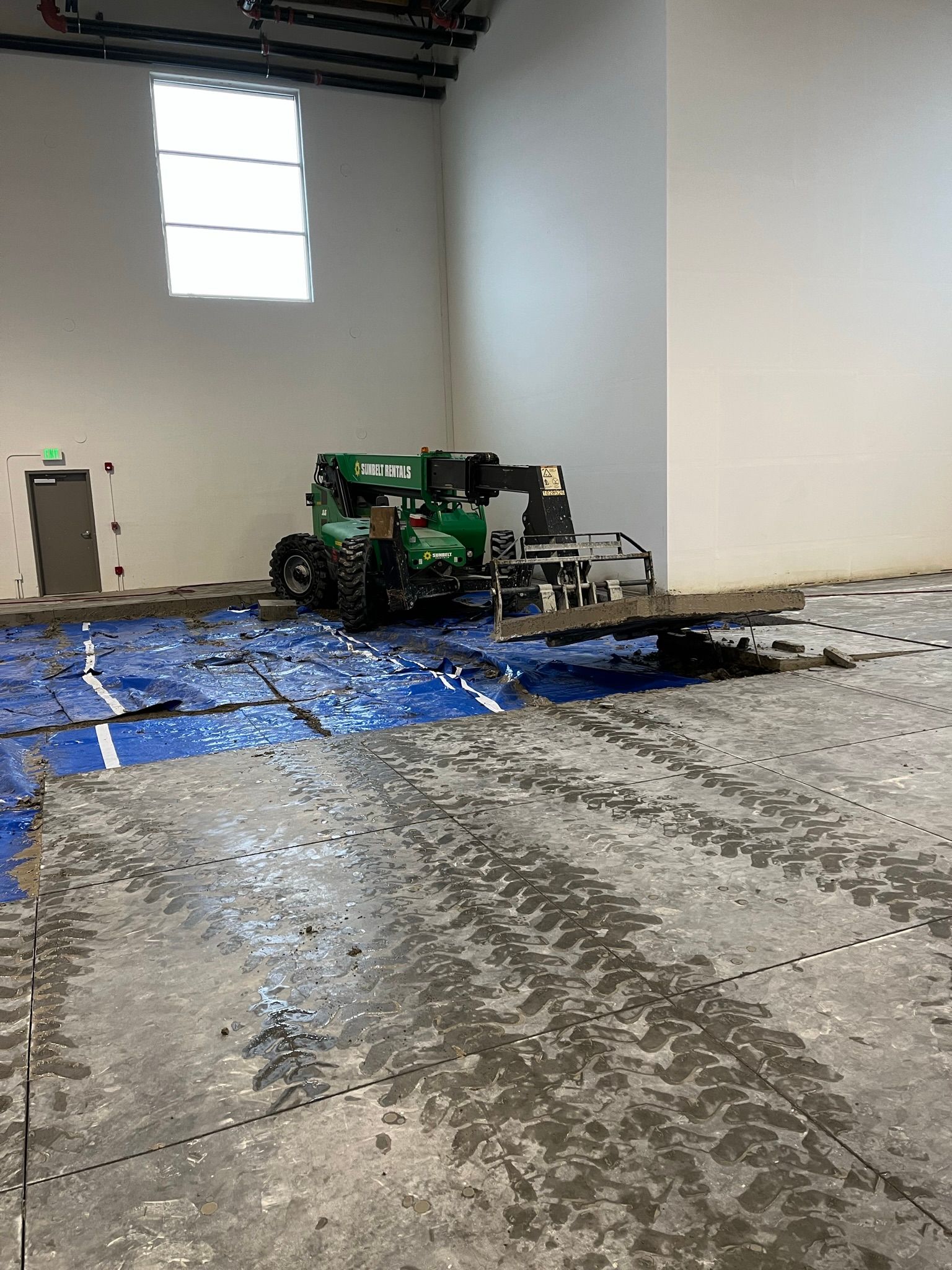 A green tractor is sitting on top of a concrete floor in a large room.