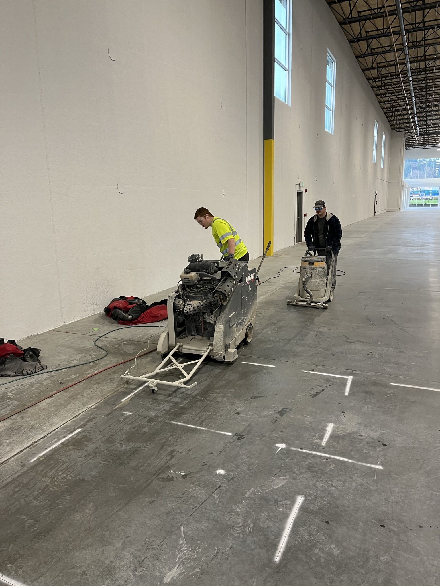 A man is cutting concrete in a large warehouse with a machine.